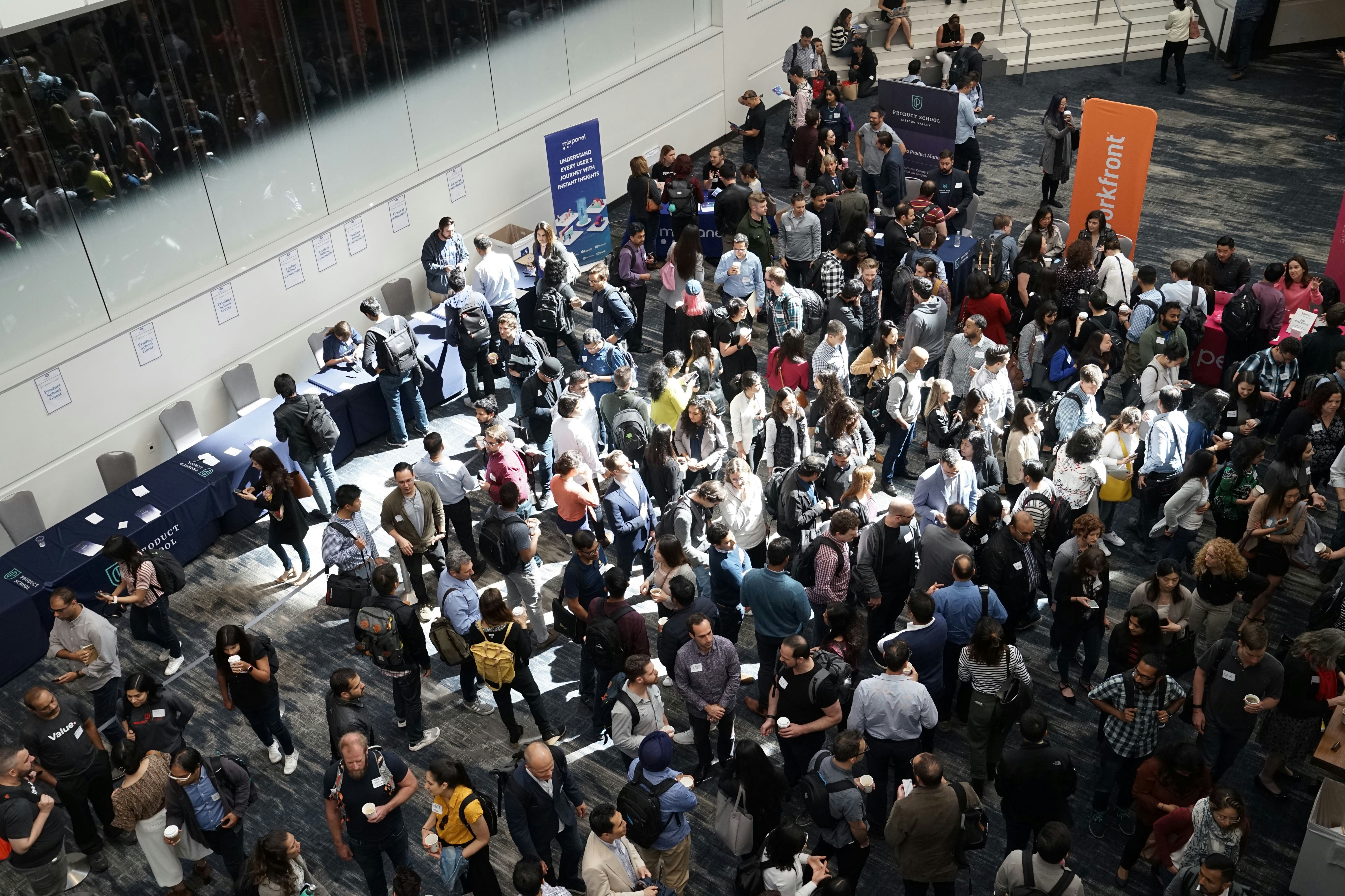 Aerial view of a busy trade show floor with attendees networking around exhibition booths and branded stands